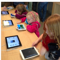 Des élèves en bas âge sont assis avec des tablettes électroniques à la main. Ils ont l'air de découvrir de nouvelles applications voire de nouveaux jeux pour certains sur celles-ci.