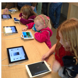 Des élèves en bas âge sont assis avec des tablettes électroniques à la main. Ils ont l'air de découvrir de nouvelles applications voire des nouveaux jeux pour certains sur celles-ci.