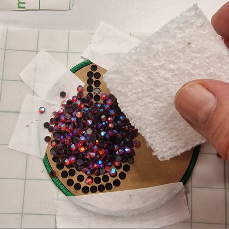 Brushing stones into the holes. The template is taped to an embroidery patch.